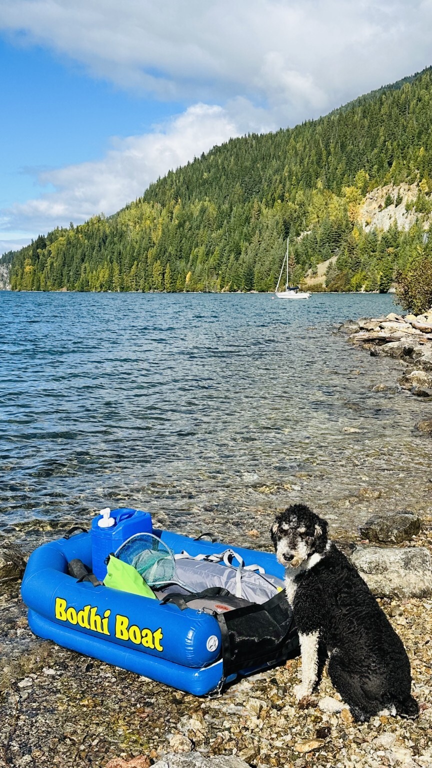 Bodhi Boat loaded with camping gear on a lakeshore with Bodhi standing beside it